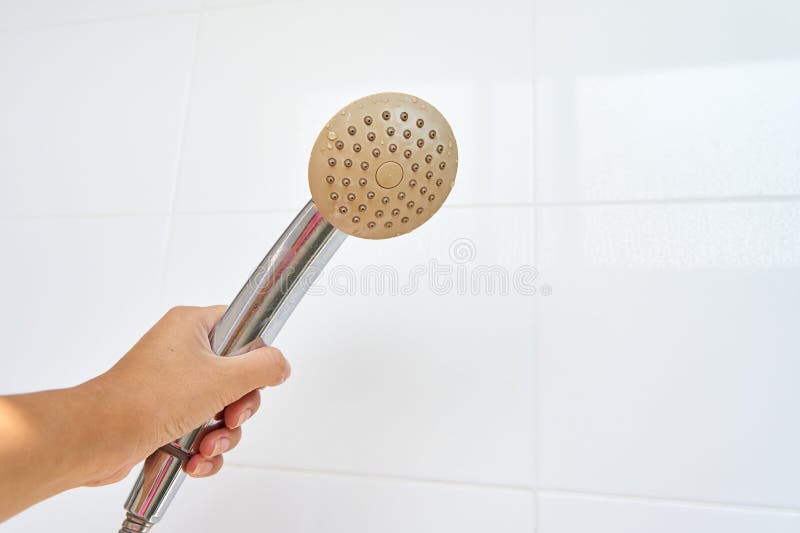 Woman holding in hand corroded limescale calcified old shower head hanging from a stand inside cabin royalty free stock photos