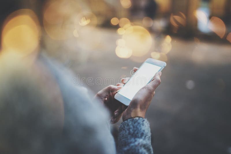 Woman holding hands smartphone in night atmospheric city.Female hands using mobile phone.Closeup on blurred background