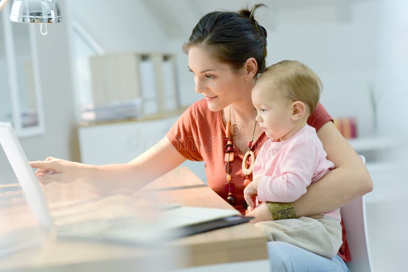 Woman holding her baby and working on laptop stock photo Woman holding her baby and working on laptop stock photo
