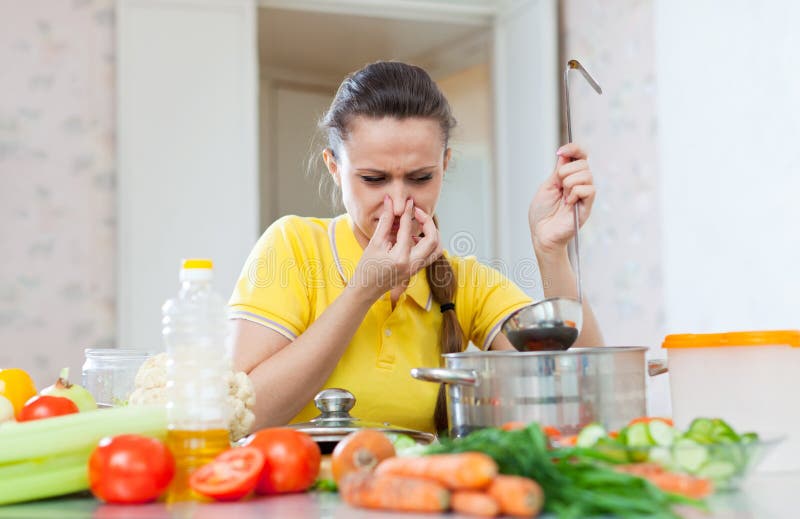Woman holding her nose because of bad smell from soup in pan at kitchen