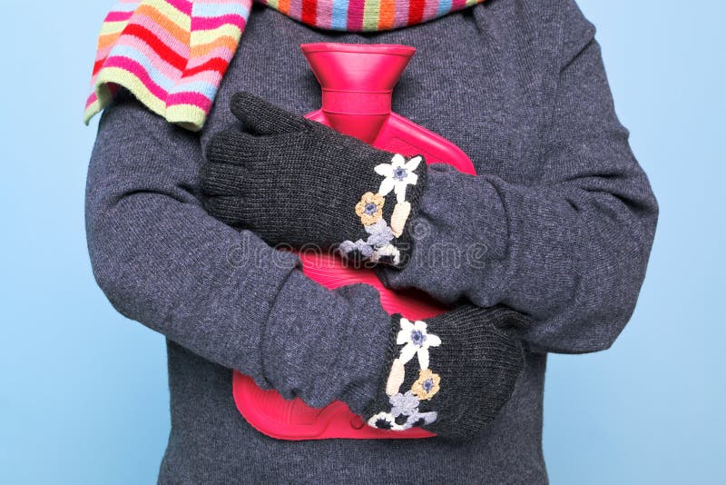 Photo of a woman holding a red hot water bottle to her chest whilst wearing hand kniitted woolen gloves trying to keep warm, good image for winter illness or warmth related themes. Photo of a woman holding a red hot water bottle to her chest whilst wearing hand kniitted woolen gloves trying to keep warm, good image for winter illness or warmth related themes.