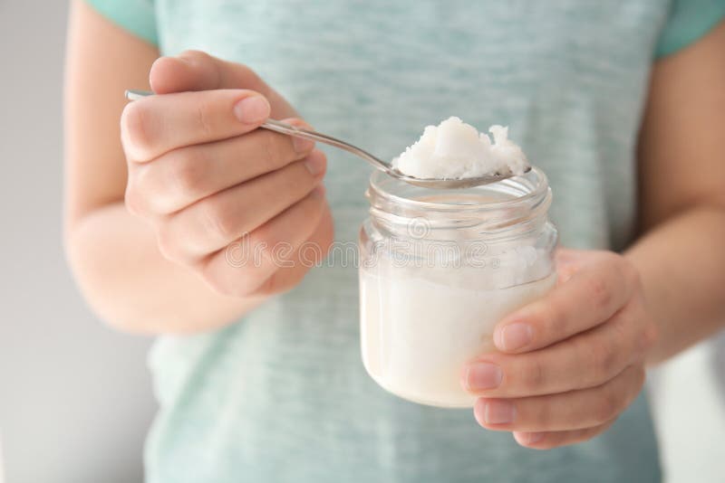 Woman holding jar and spoon with coconut oil, closeup