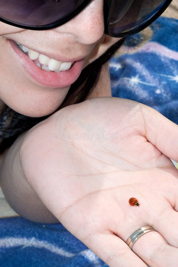 A young woman holding a ladybug in the palm of her hand at the beach.