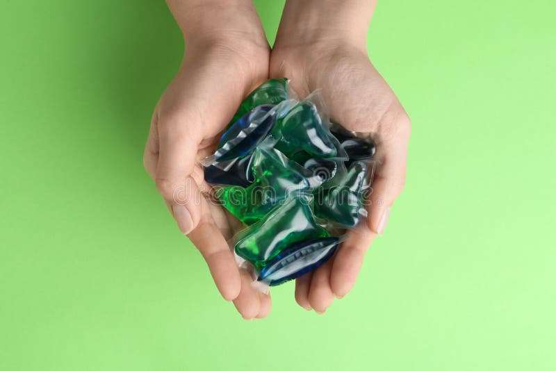 Woman holding laundry capsules on green background, top view