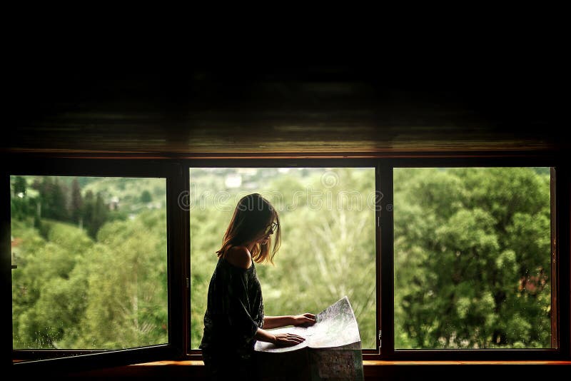 woman holding map sitting at window with view at amazing mountains in wooden house, planning summer travel or architect