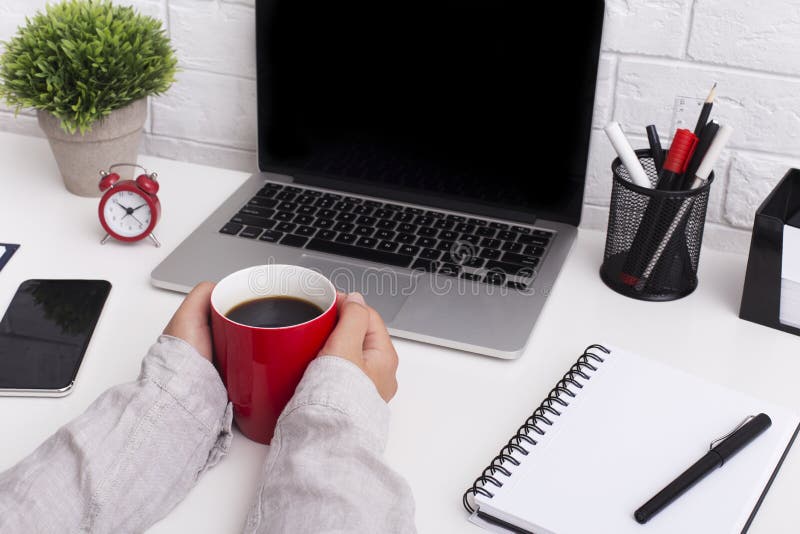 Colored atmosphere. Woman holding red cup with coffee in front of laptop with blank screen on office table