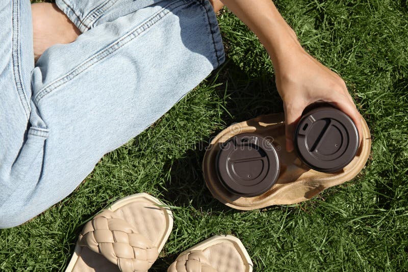 Woman holding takeaway cardboard coffee cups with plastic lids on green grass, top view royalty free stock photography