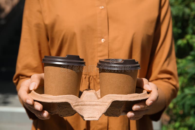 Woman holding takeaway cardboard coffee cups with plastic lids outdoors, closeup stock photography