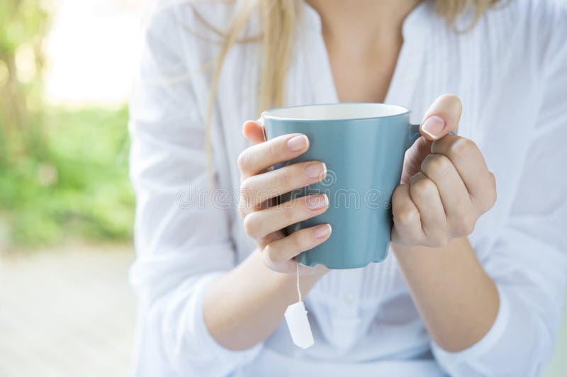 Closeup shot of a woman holding tea mug. Close up of young woman's hand holding a cup of hot tea. Relaxed girl drinking tea. Shallow depth of field with focus on tea mug.