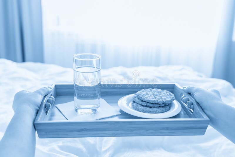 Woman Holding Tray with Diet Breakfast of Crackers and Water on a Bed