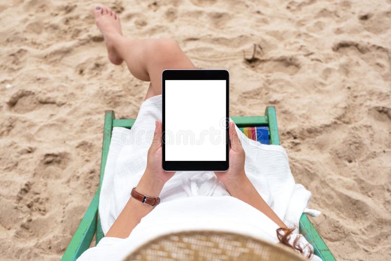 A woman holding and using a black tablet pc with blank desktop screen while laying down on a beach chair stock photos A woman holding and using a black tablet pc with blank desktop screen while laying down on a beach chair stock photos