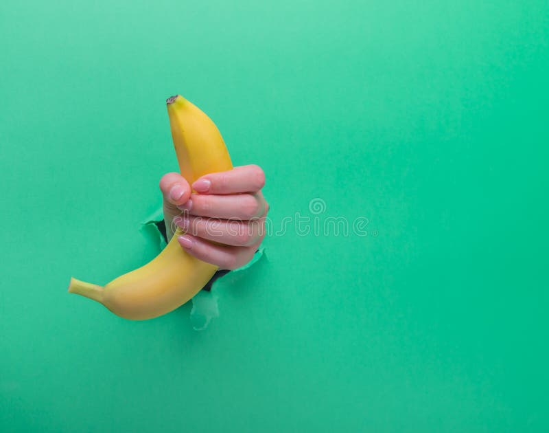 A woman holds a banana in her hand, inserted through a hole in torn green p...