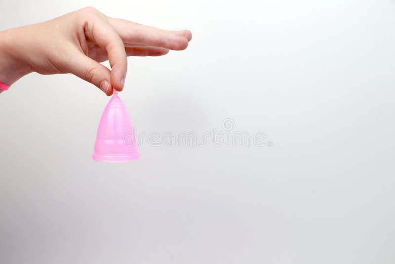A woman holds a menstrual cup in her hand on a pink background. The concept of women`s health, hygiene, alternatives pads and royalty free stock photo A woman holds a menstrual cup in her hand on a pink background. The concept of women`s health, hygiene, alternatives pads and royalty free stock photo