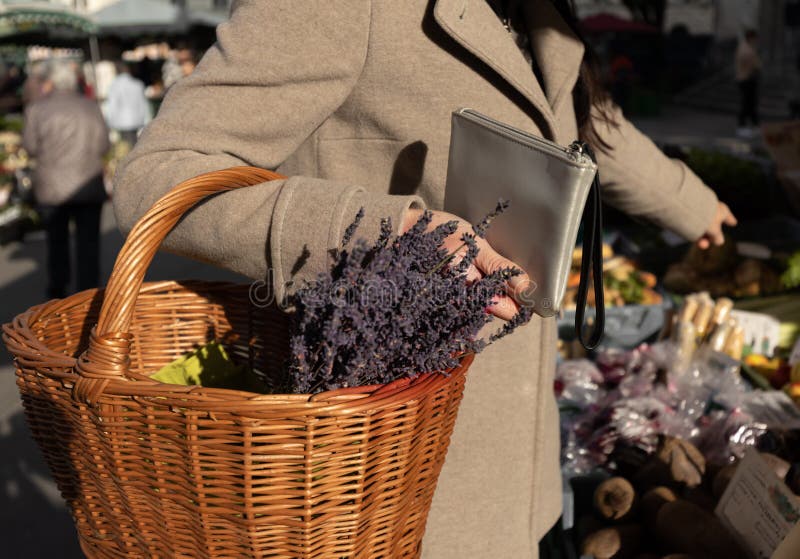 A woman holds a purse and a basket of lavender in her hands and points to the product she wants to buy. High quality photo