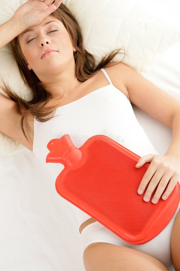 Young woman lying on bed with hot water bottle on her stomach. Young woman lying on bed with hot water bottle on her stomach