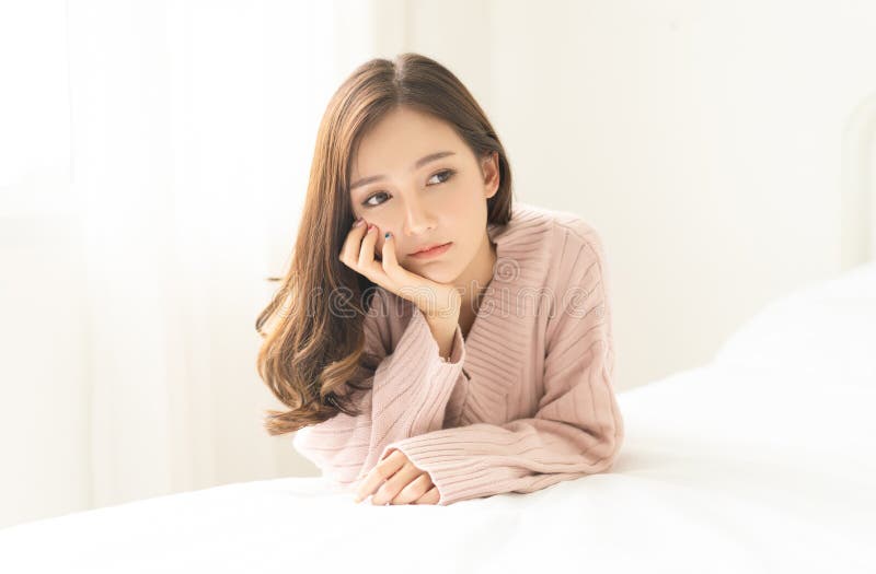 Woman indoor portrait. Closeup of pensive young Asain woman in warm knitted pink clothes in the bedroom. Negative human facial royalty free stock images Woman indoor portrait. Closeup of pensive young Asain woman in warm knitted pink clothes in the bedroom. Negative human facial royalty free stock images