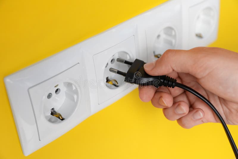 Woman Inserting Plug into Power Socket on Yellow Wall, Closeup
