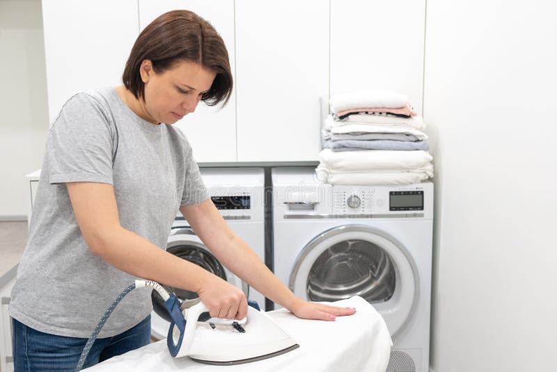 Woman Ironing on Board in Laundry Room with Washing Machine on ...