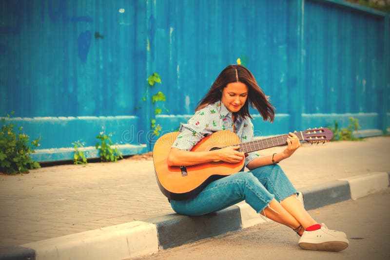 Woman in jeans sits on a road curb and plays the guitar stock photography Woman in jeans sits on a road curb and plays the guitar stock photography
