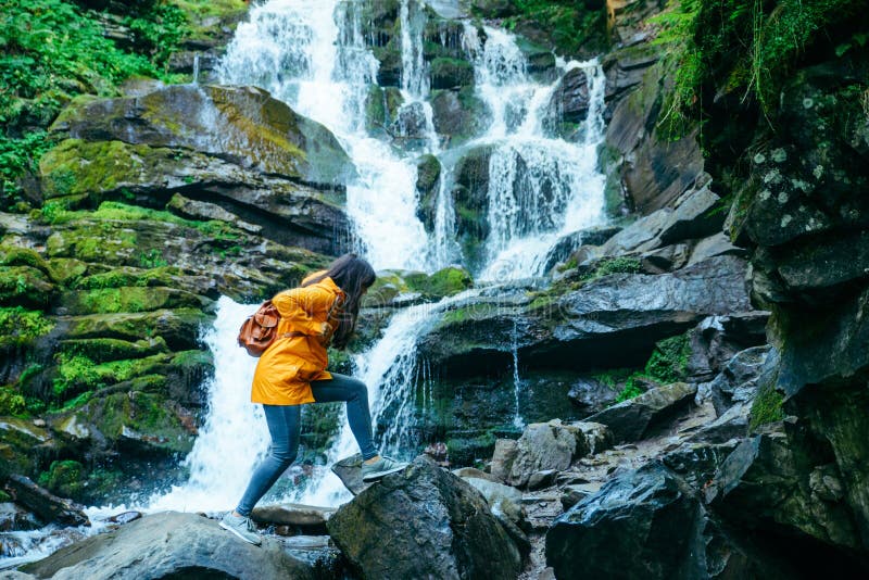 Woman jump from rock to rock in forest. water fall on background