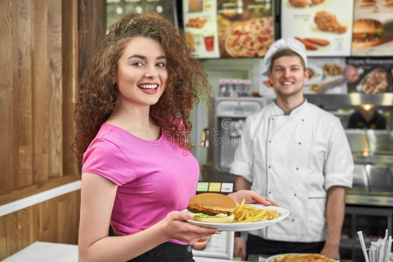 Woman keeping plate with fast food and smiling in cafe. royalty free stock photos Woman keeping plate with fast food and smiling in cafe. royalty free stock photos
