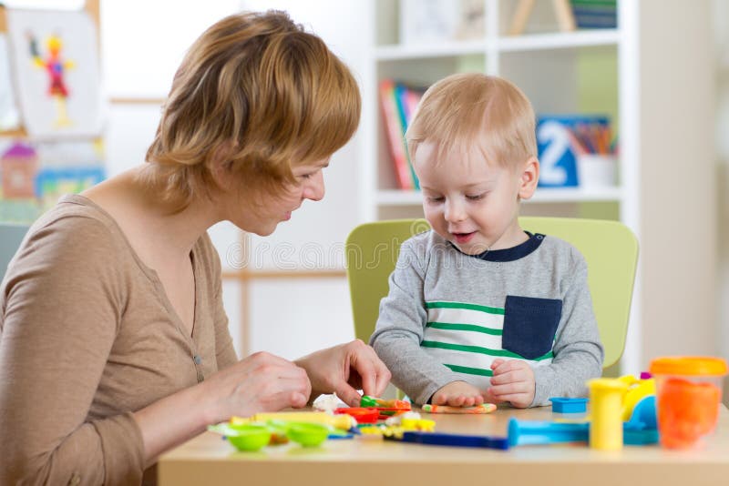 Woman and kid boy playing with plasticine at table in nursery room