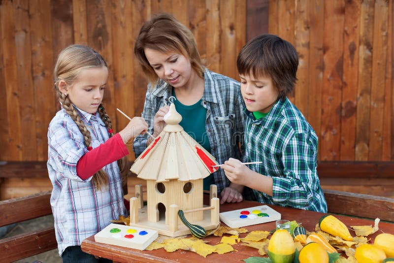 Woman with kids painting the bird house - preparing for winter stock image Woman with kids painting the bird house - preparing for winter stock image
