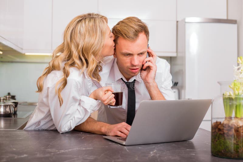 Woman Kissing Her Husband On Cheek While He Is Talking On The Phone