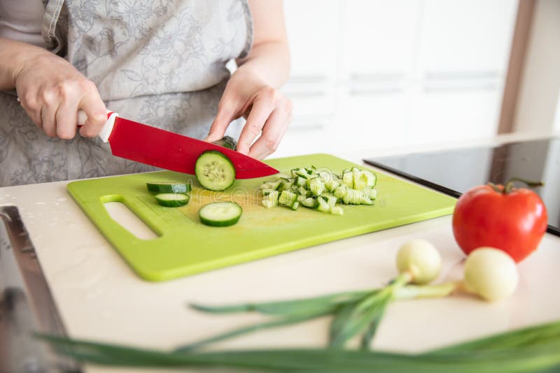 Woman in  kitchen apron cuts cucumber on the cutting board with red knife