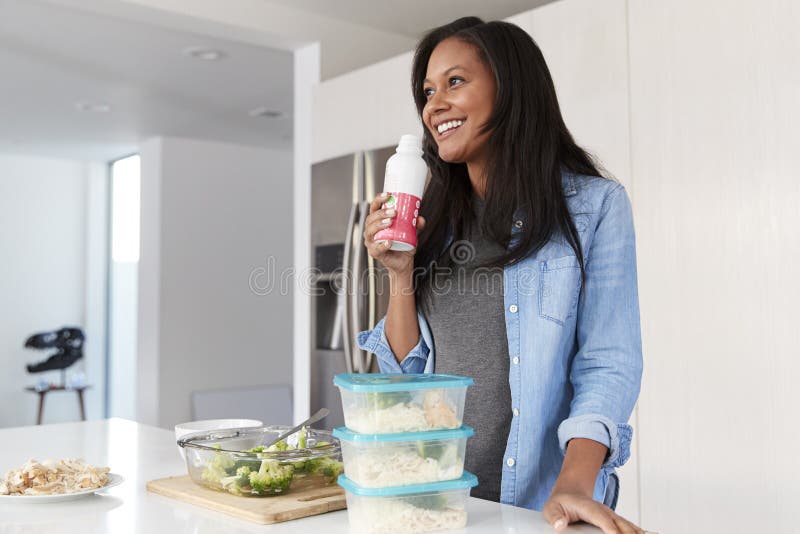 Woman In Kitchen Preparing Healthy Meal Drinking Protein Shake From Bottle