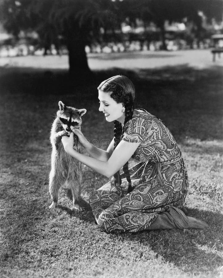 Woman kneeling on the lawn playing with a tame raccoon