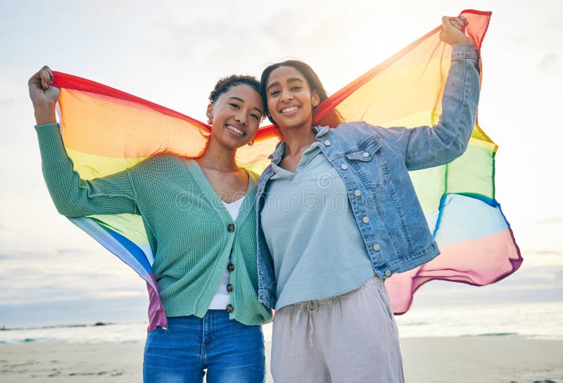Woman, lesbian couple and pride flag on beach together in happiness for LGBTQ community or rights. Portrait of proud and stock images
