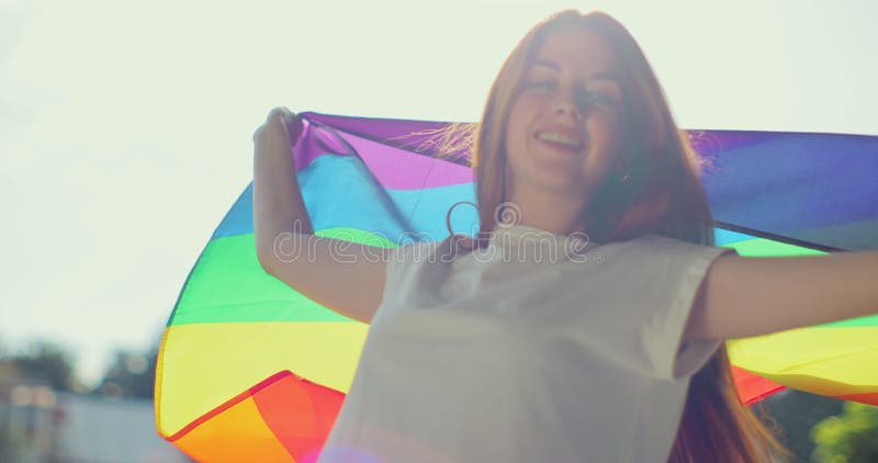 Woman lesbian holds a LGBT gender identity flag on a background. Smiled young woman spinning around with lgbt flag on stock photo