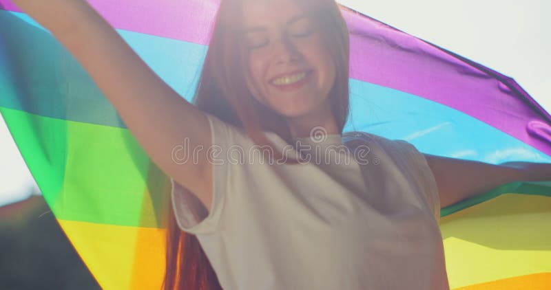 Woman lesbian holds a LGBT gender identity flag on a background. Smiled young woman spinning around with lgbt flag on stock photos