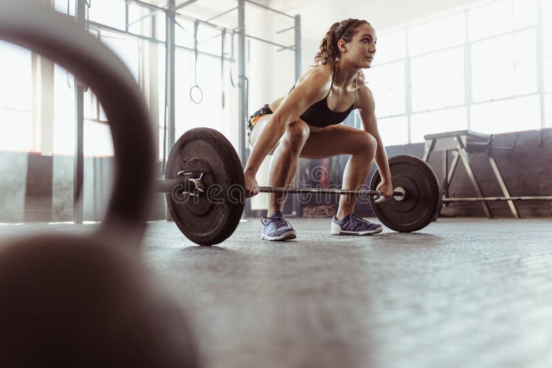 Young women lifting a barbell at the gym. Fit female athlete exercising with heavy weights at cross training gym. Young women lifting a barbell at the gym. Fit female athlete exercising with heavy weights at cross training gym.