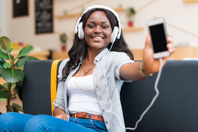 Woman listening music with headphones and showing smartphone while sitting in cafe royalty free stock images Woman listening music with headphones and showing smartphone while sitting in cafe royalty free stock images