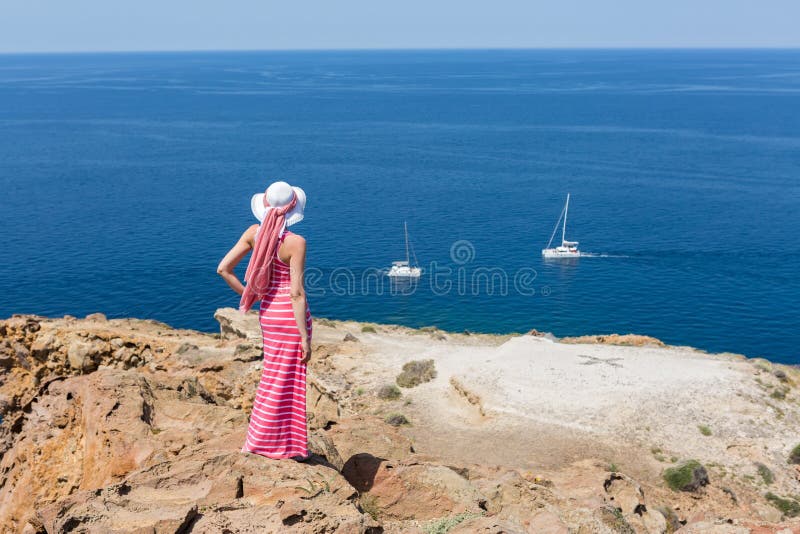 Woman in a long summer dress standing on a cliff sea.