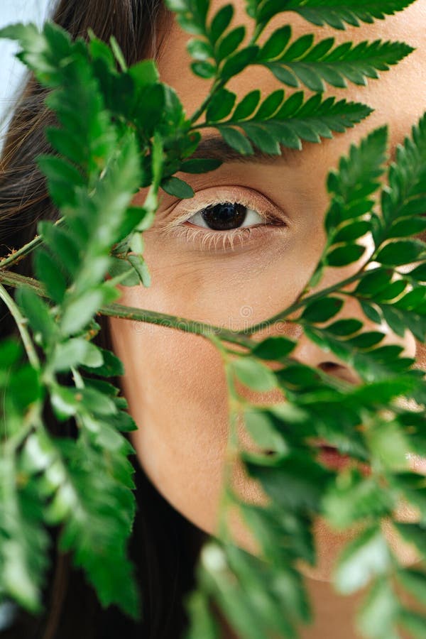 Woman looking through fern at camera with eye with vitiligo eyelashes. Close up