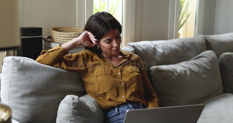 Woman looking at laptop on lap while lounging on sofa stock video footage