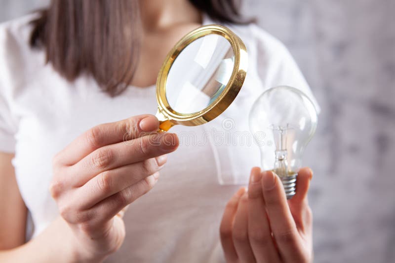 Woman Looking at a Light Bulb with a Magnifying Glass Stock Photo