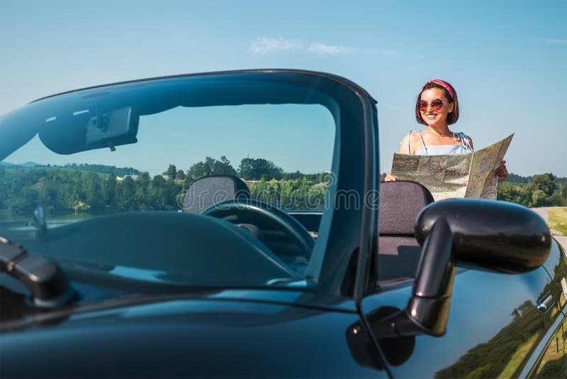 Woman looking a right road in the roadmap during her auto travel in the convertable cabriolet car. Traveling and navigation