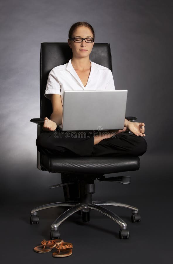 Woman in lotus pose in chair with laptop.