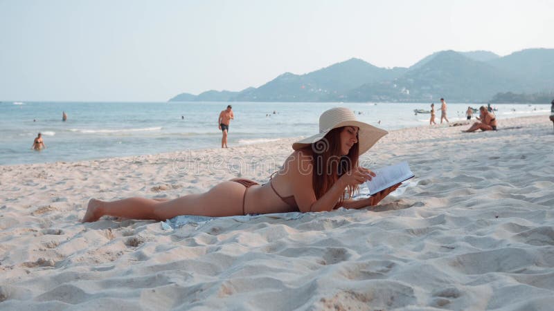 Woman lying on beach enjoys serenity of sea while reading book embracing simple pleasure of reading book. As she reading