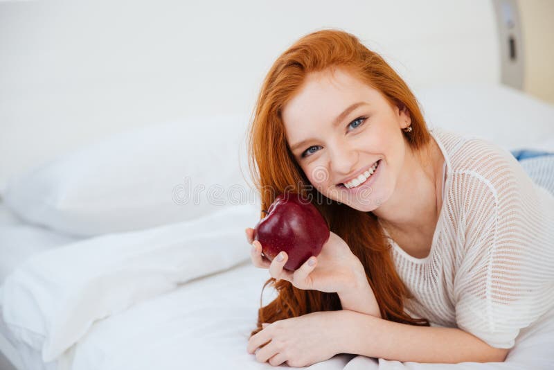 Woman lying on the bed and holding red apple