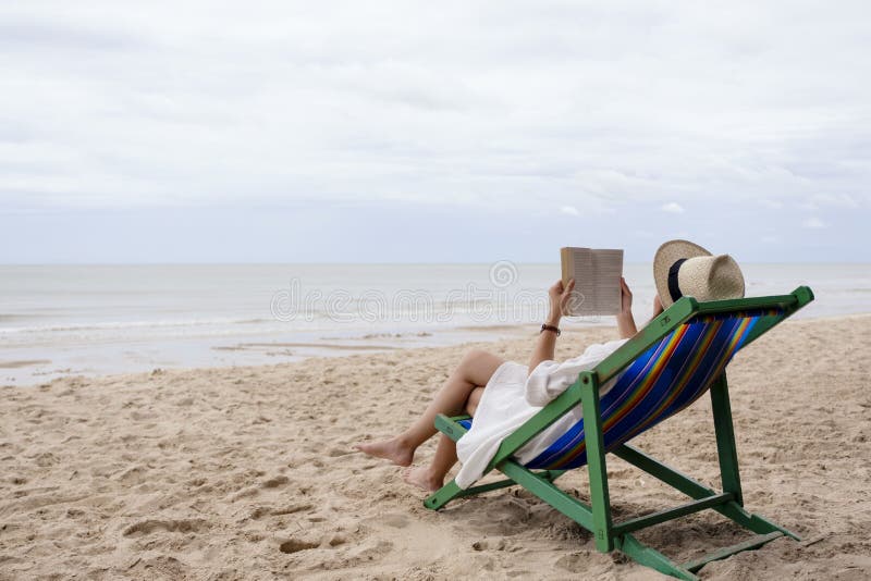 A woman lying down and reading book on the beach chair with feeling relaxed