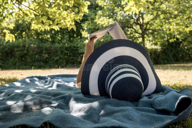 Woman lying on a rug in the shade of a tree reading a book