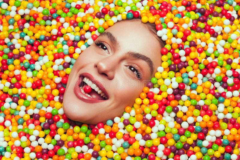 Mladá modelka všetky posedenie s cukríkmi pózuje s candy v ústach pri pohľade hore.