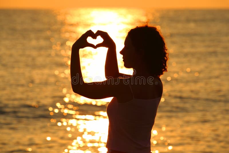 Woman makes heart by hands at sunset