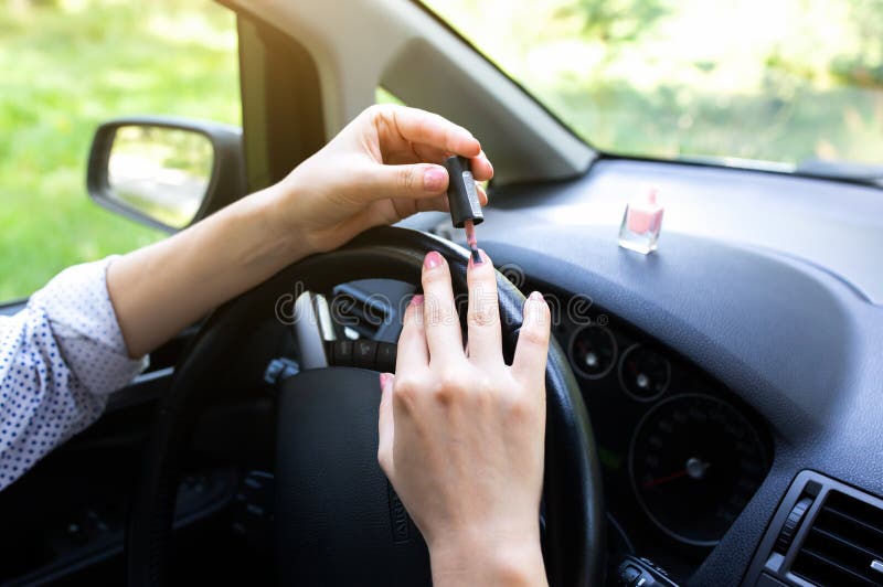 Woman is making manicure in the car. Girl applying  nail polish behind the wheel. Dangerous situation on the road