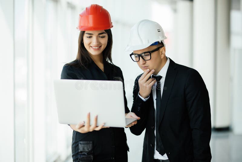 Woman and man entrepreneur and architect in hemlet at business meeting, looking at the laptop on building plans royalty free stock image Woman and man entrepreneur and architect in hemlet at business meeting, looking at the laptop on building plans royalty free stock image